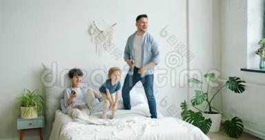 男人和孩子在床上<strong>蹦蹦</strong>跳跳，而女孩妈妈在用智能手机